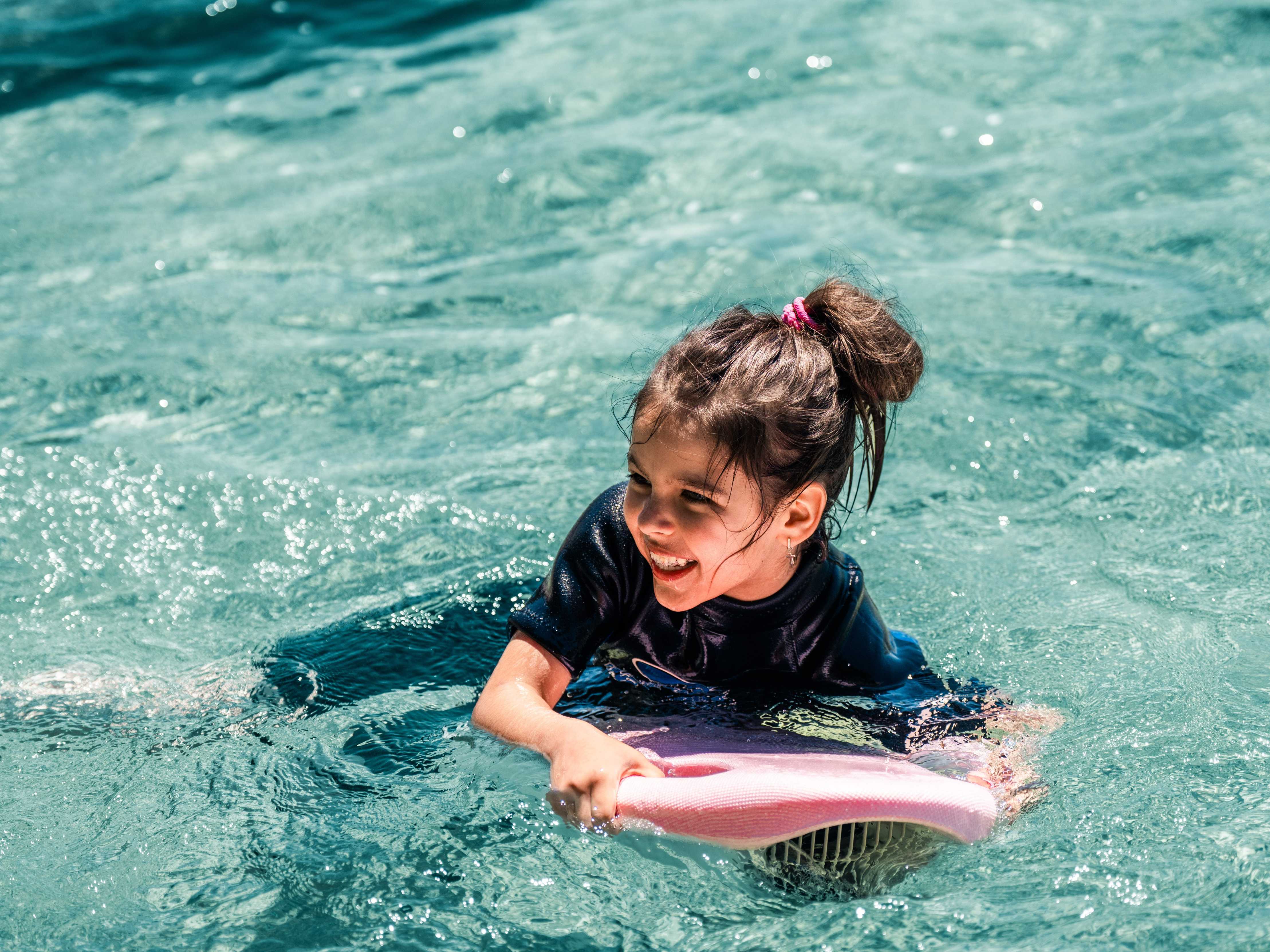 A little girl uses a portable water toy ASIWO MAKO Electric Kickboard in the swimming pool