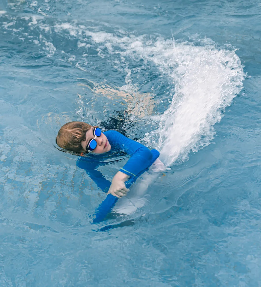Child swimming in the pool, holding the ASIWO MAKO electric kickboard, with water splashing behind them while wearing blue swim gear and goggles