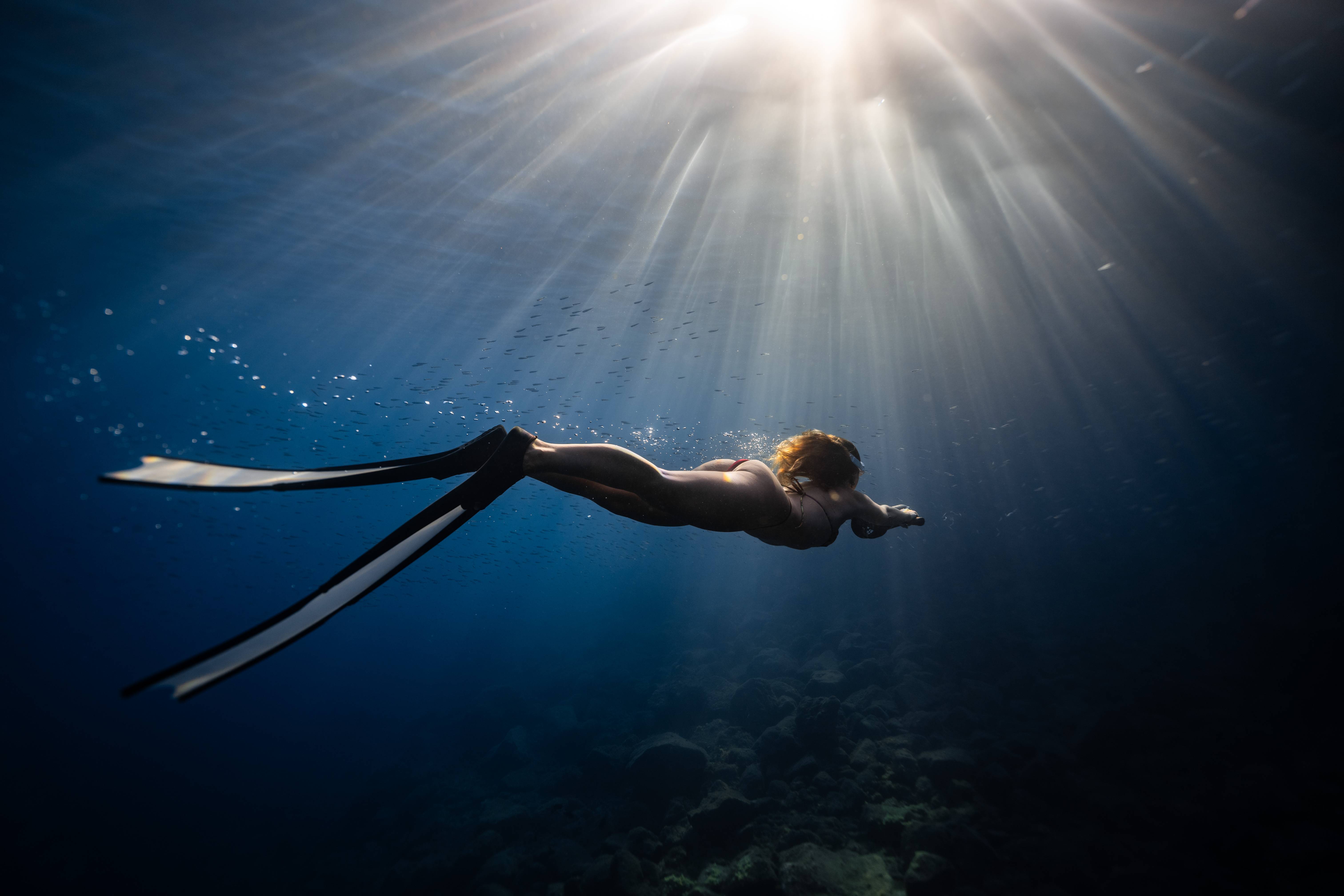 Snorkeler swimming underwater with long fins as sunlight streams through the ocean above