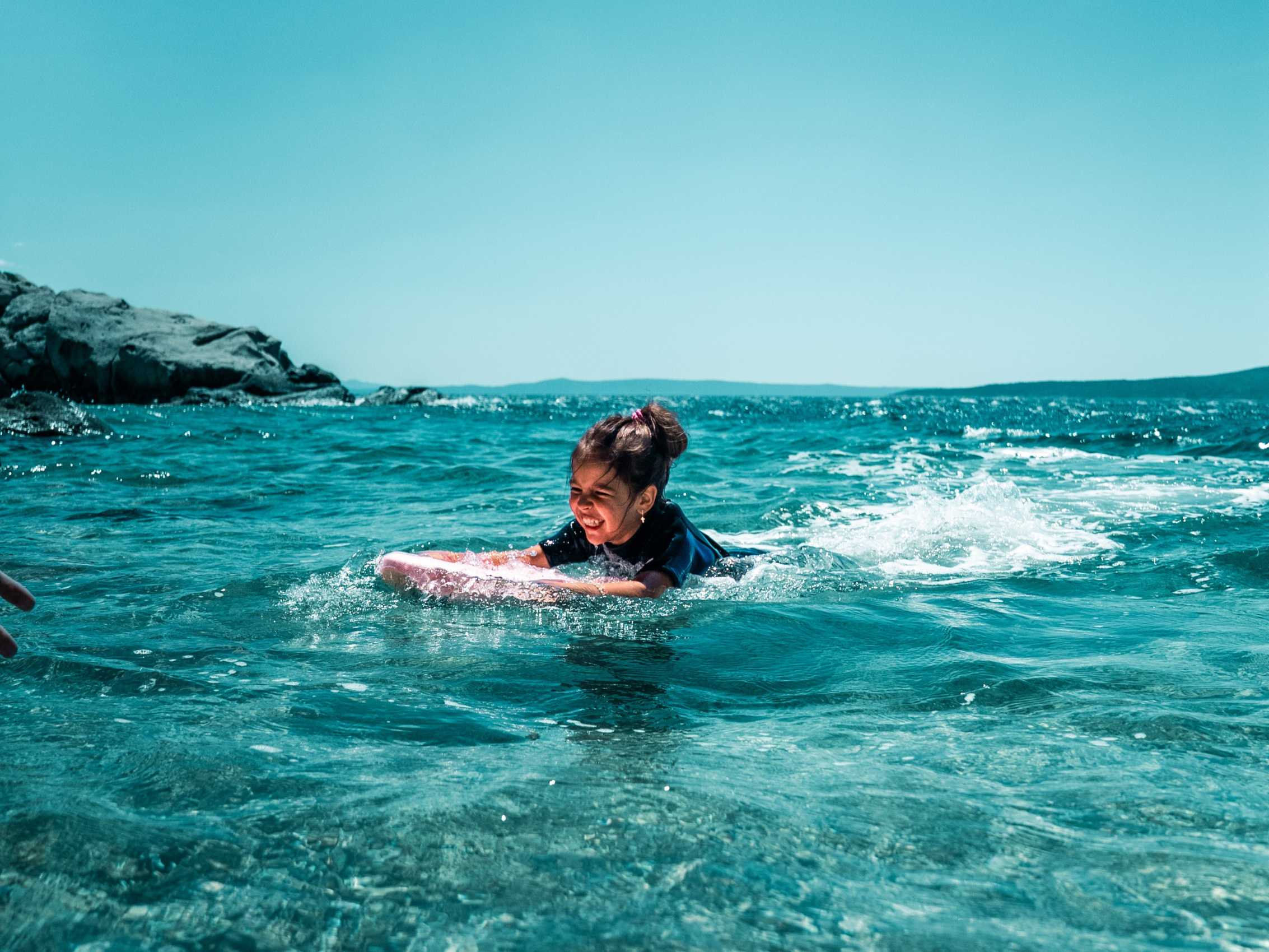 Child riding a Electric Kickboard in small ocean waves, navigating light surf and current near rocky shoreline