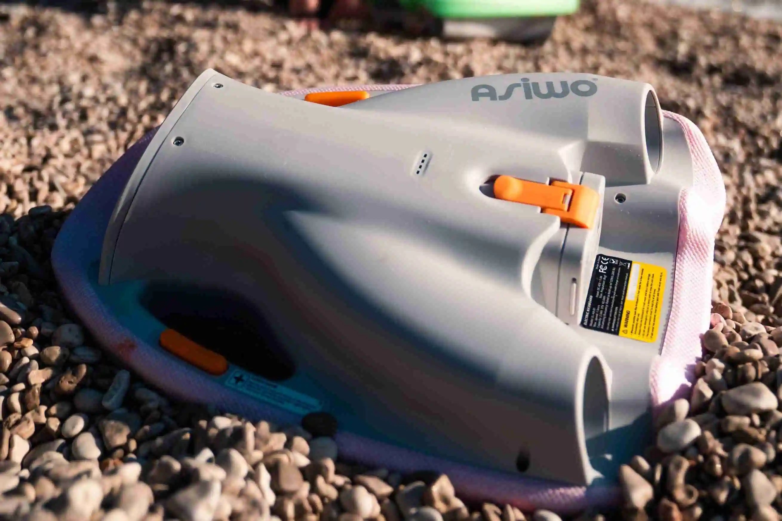 ASIWO MAKO electric kickboard underwater scooter placed on rocky beach, compact gray water propulsion device with orange accents