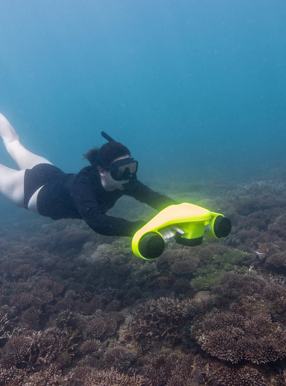 A person snorkeling or diving underwater using a bright yellow and black ASIWO Manta underwater scooter near coral.