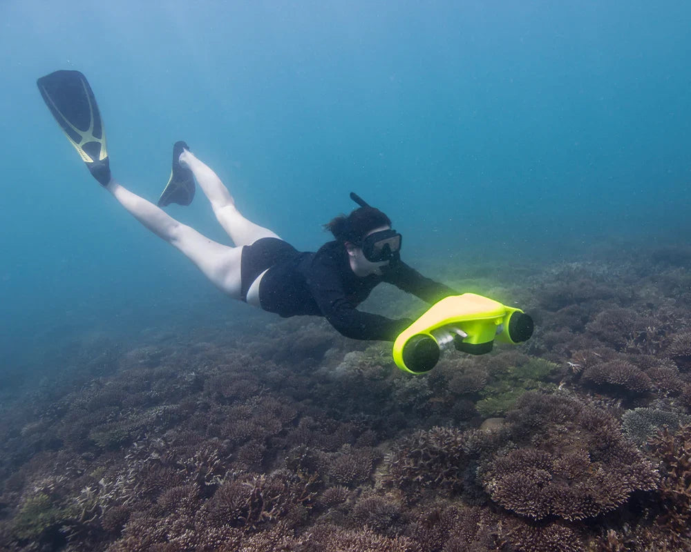 Snorkeler using the ASIWO Manta underwater scooter and waering a snorkeling maskto glide above a coral reef in clear ocean water.