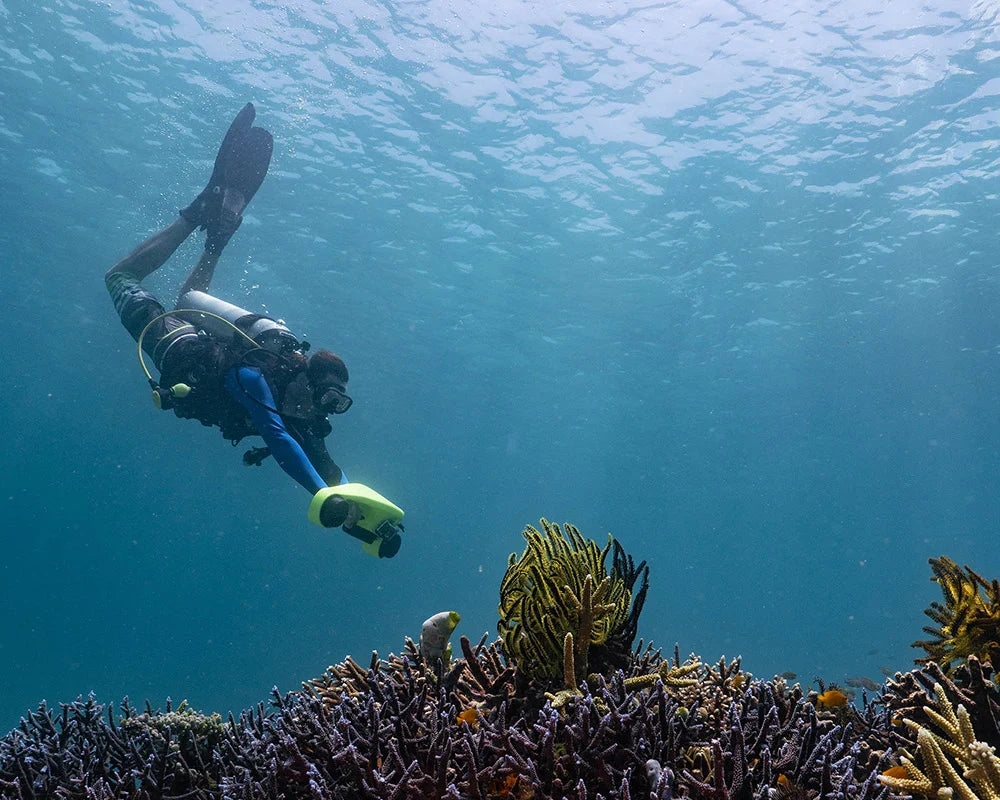 A scuba diver using a green underwater scooter above a coral reef.
