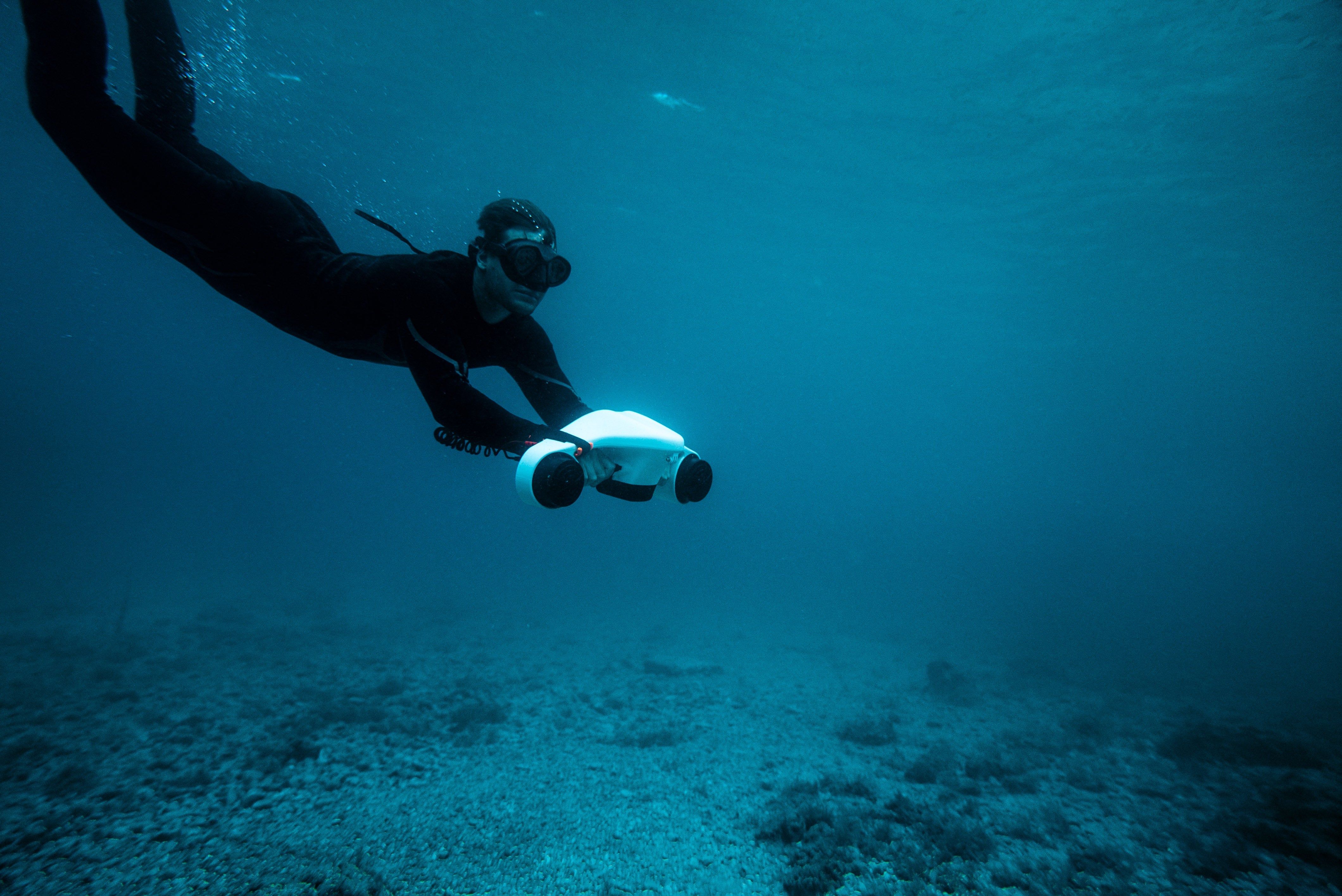 Freediver cruising underwater with the ASIWO Manta underwater scooter above a rocky seabed.