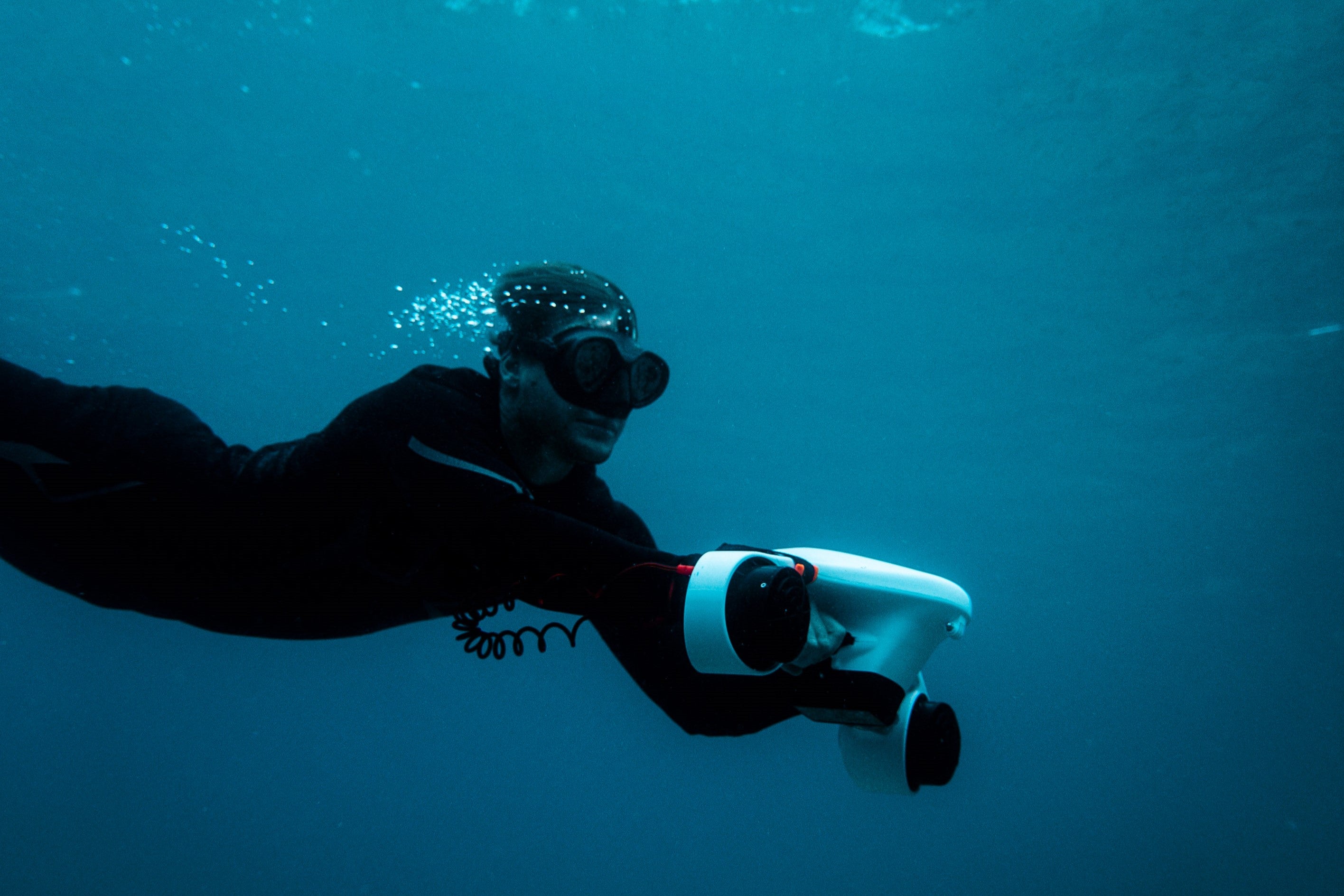 ASIWO Manta underwater scooter propelling a diver smoothly through clear blue water, with bubbles trailing behind and a streamlined dual-thruster design visible