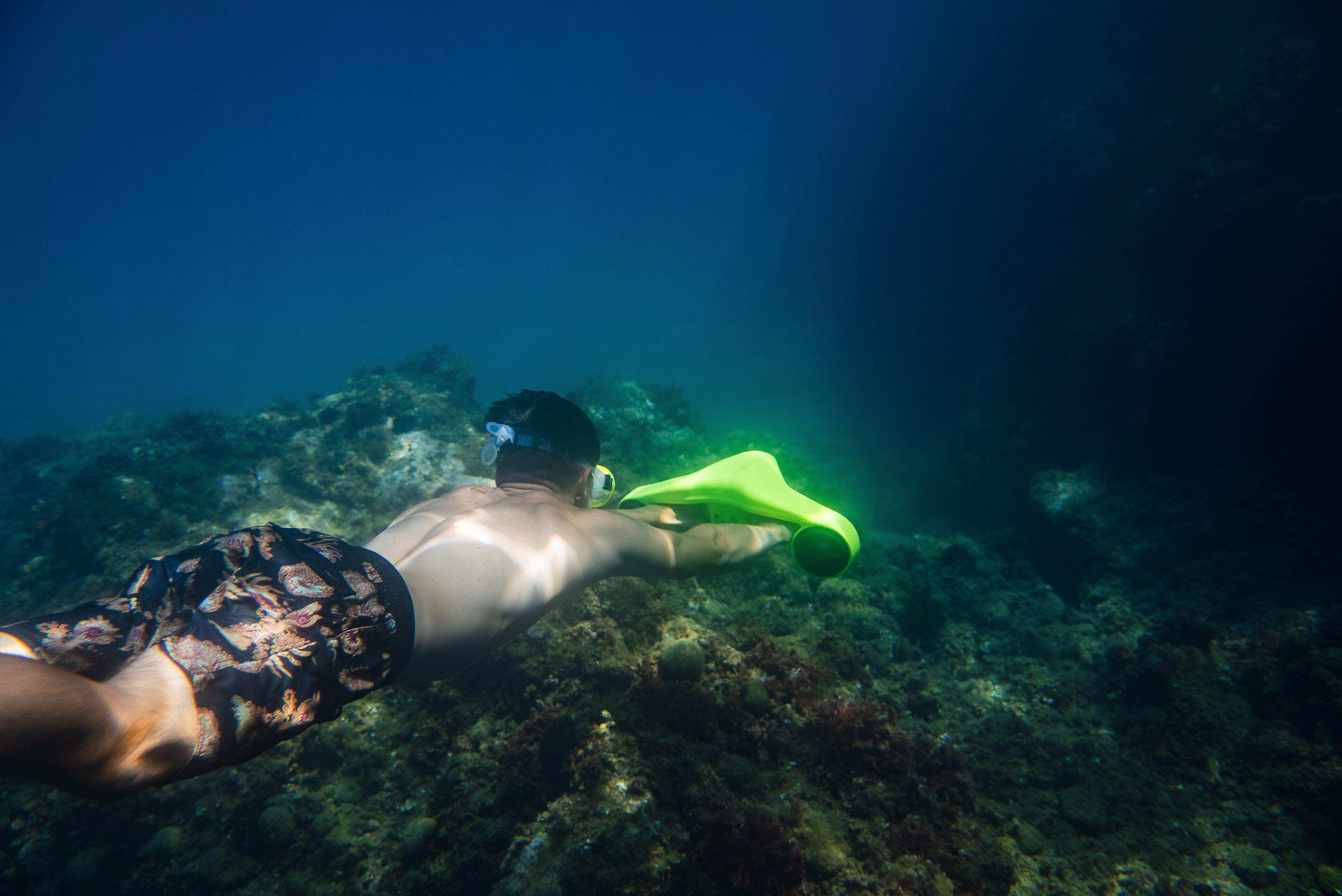A snorkeler gliding underwater with an underwater scooter above a rocky seabed.