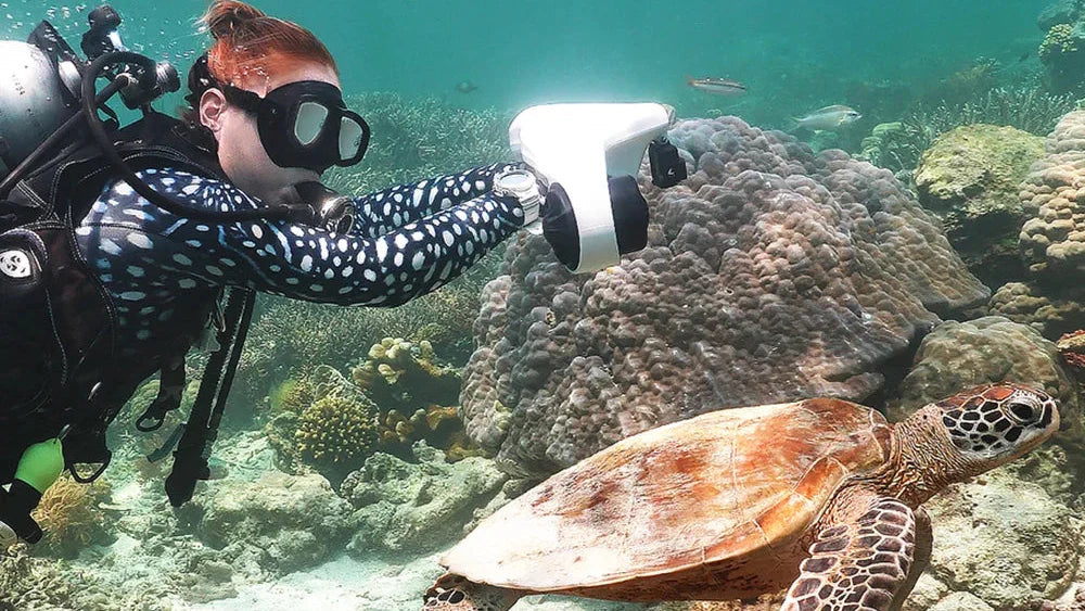 ASIWO Manta underwater scooter used by a scuba diver exploring a coral reef alongside a sea turtle in clear tropical water