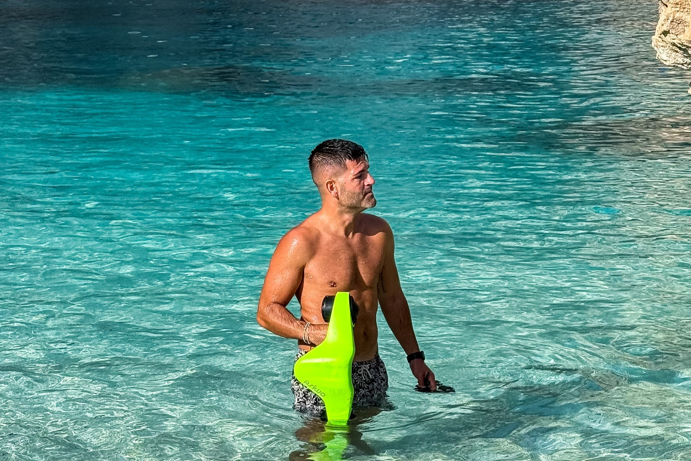Man standing in clear turquoise water holding a green ASIWO Manta underwater scooter.