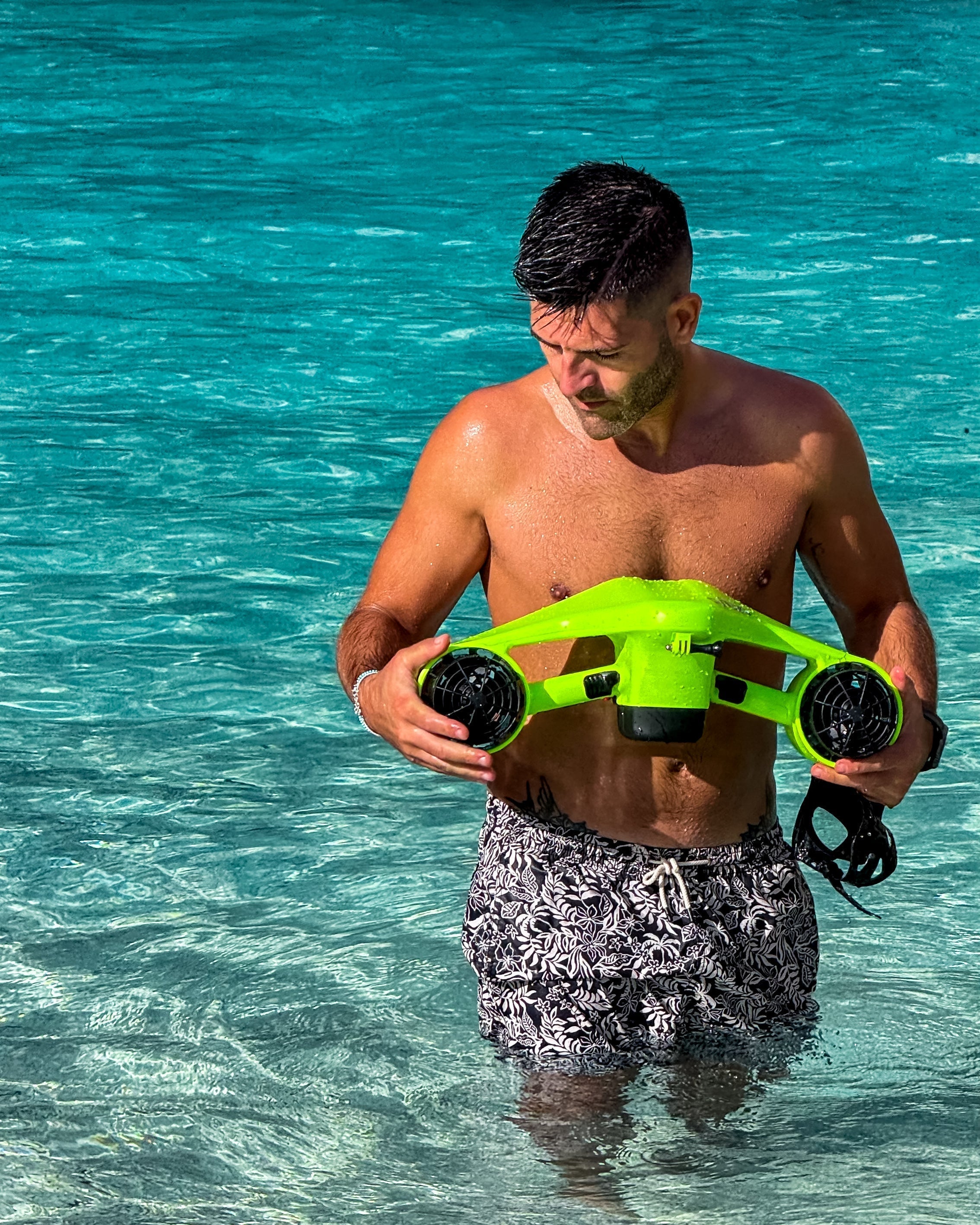  A man standing in shallow, clear water, holding a green Asiwo Manta underwater scooter.