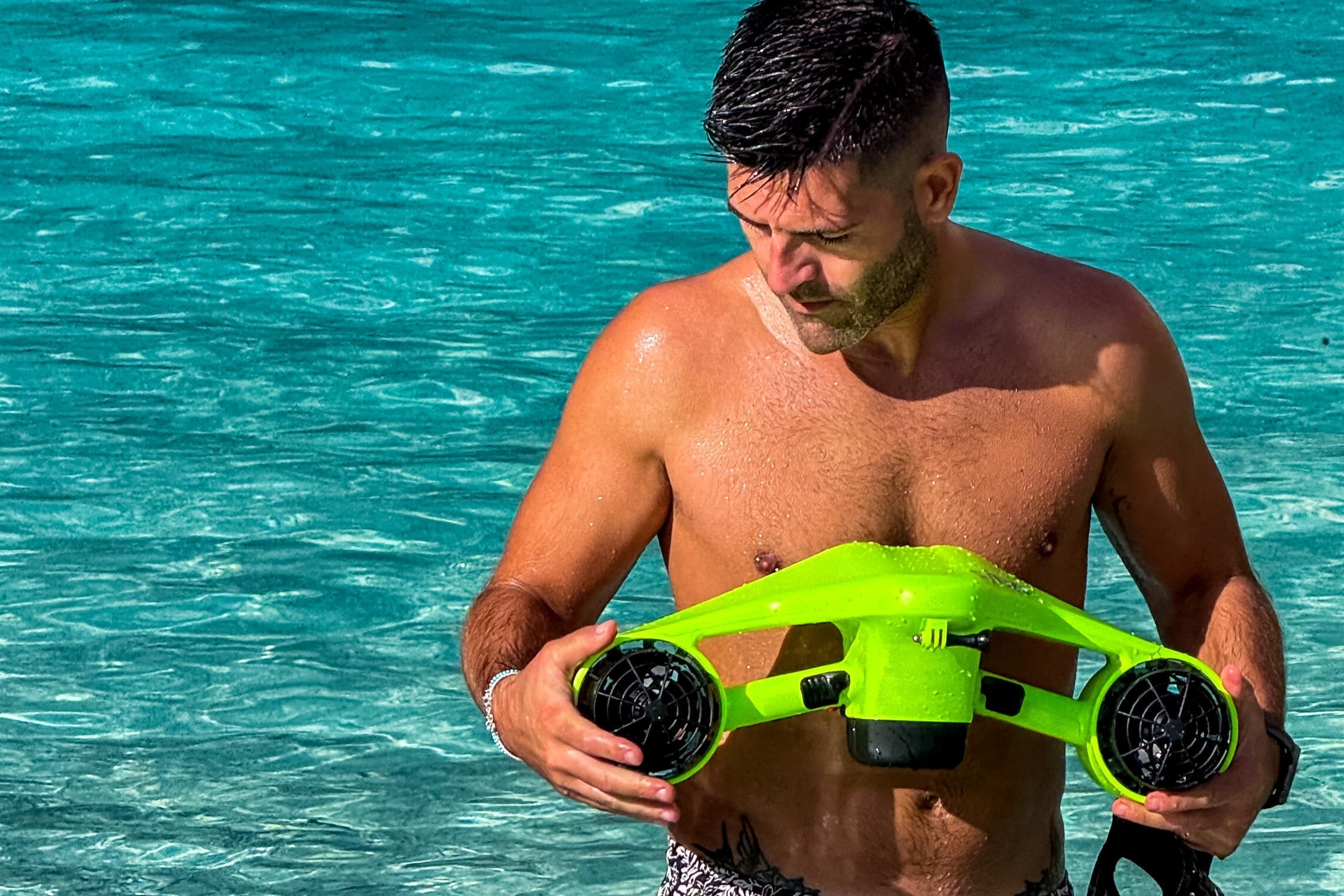 Person holding ASIWO Manta underwater scooter in bright green while standing in clear shallow ocean water