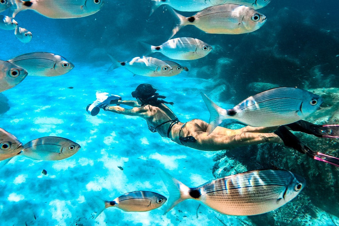 A snorkeler gliding underwater with an underwater scooter among a school of fish.